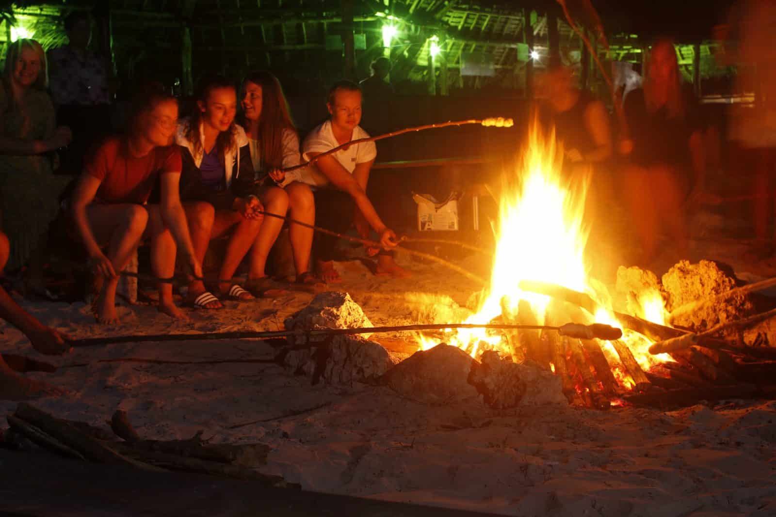 Aftenhygge på stranden: unge sidder ved bål og rister skumfiduser – oplevelse fra Zanzibar Højskole i udlandet grupperejse sabbatår